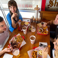 photograph of smiling people eating barbecue at a wooden table