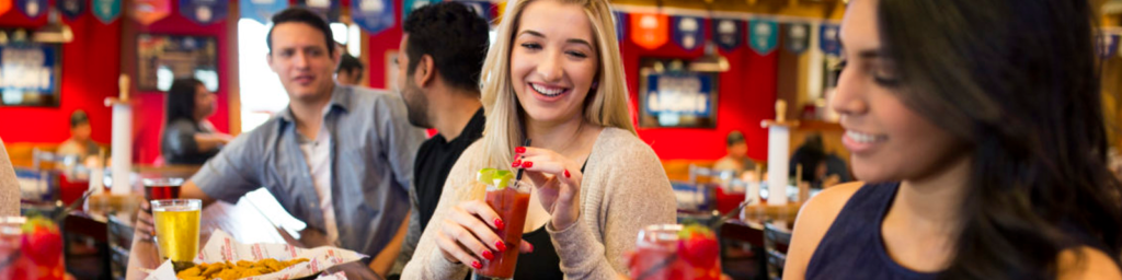A smiling woman drinks a bloody Mary against a red backdrop