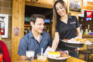 photograph of smiling server serving brisket and corn to a customer