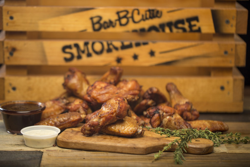 close-up photograph of barbecue chicken wings, ranch, and rosemary sprigs